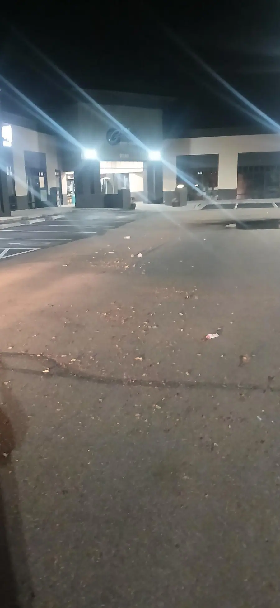 Grit and trash scattered across a strip mall parking lot at night